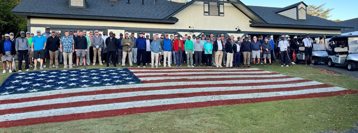 19th Annual Veterans Golf Tournament Several people stand in front of a clubhouse with a large American flag spread across the ground during the annual veterans golf tournament at the Tradition Golf Course in Charlotte.
