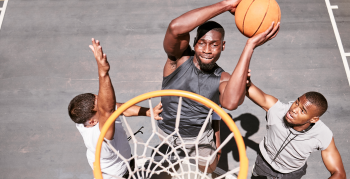 Basketball players blocking a player from dunking a ball into net to score points during a match on sports court from above . Fit athletes jumping to defend in competitive game for recreational fun.