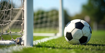 Soccer ball lies near soccer goal on grassy field. Daytime shot. Sport recreation concept. Photo captures active lifestyle. Great for sports websites, and blogs.