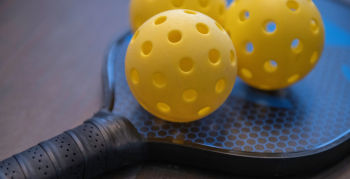 A close-up of a pickleball racket with 3 yellow pickleballs.