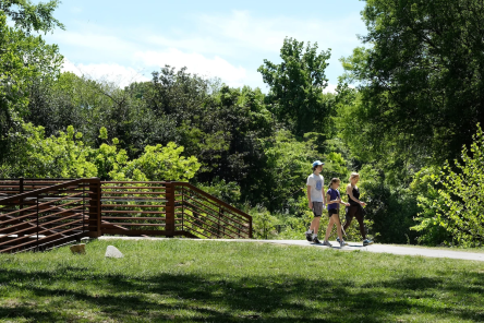 A group of people walking along Caldwell Station Greenway on a sunny day.