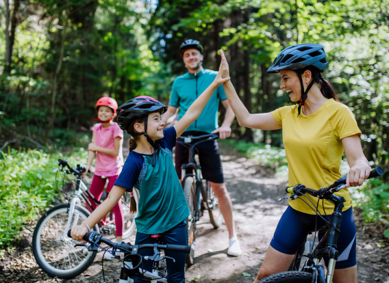 A young family with little children preapring for bike ride, standing with bicycles in nature and high fiving.